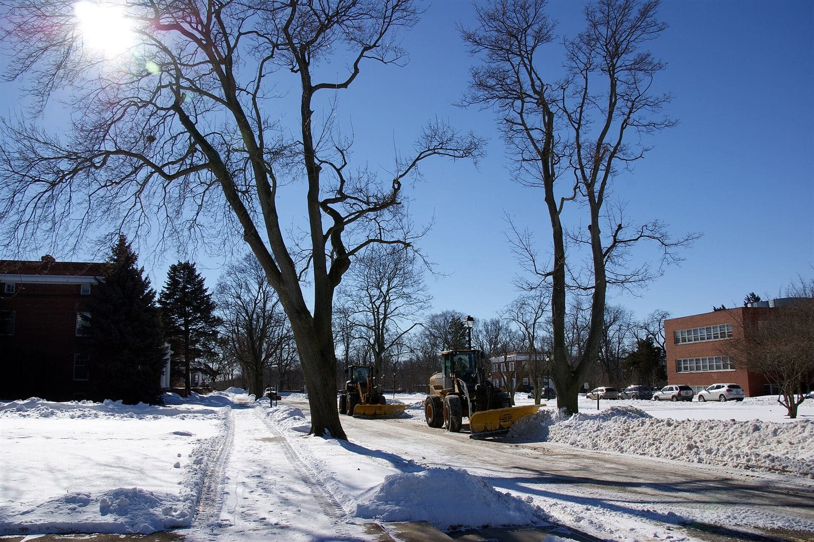 Two loaders with plow blades clearing a commercial lot and laneway after a snowfall